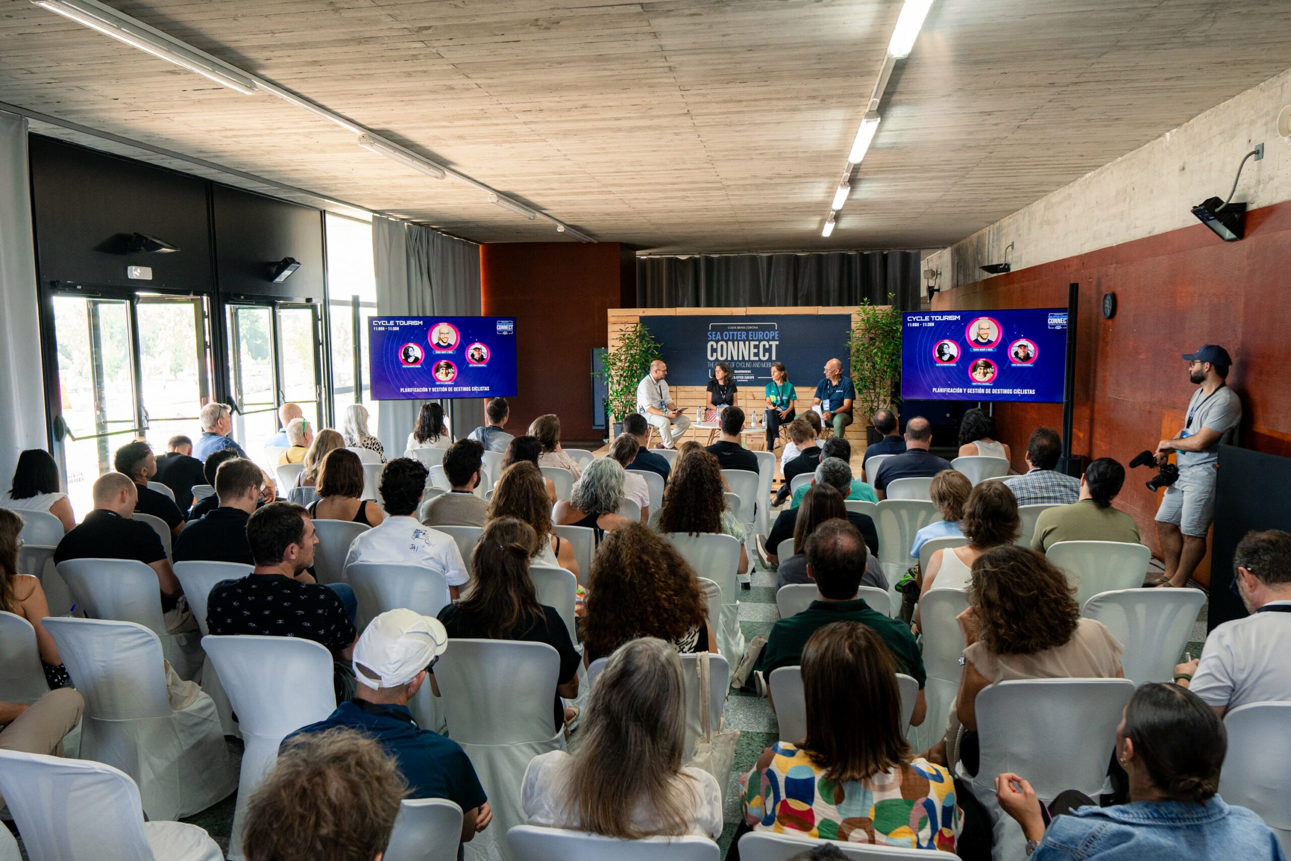 El público profesional acreditado con la acreditación PRO en una sala de conferencias escuchando una mesa redonda en el escenario de Sea Otter Europe, con diapositivas de presentación mostradas en dos pantallas grandes.