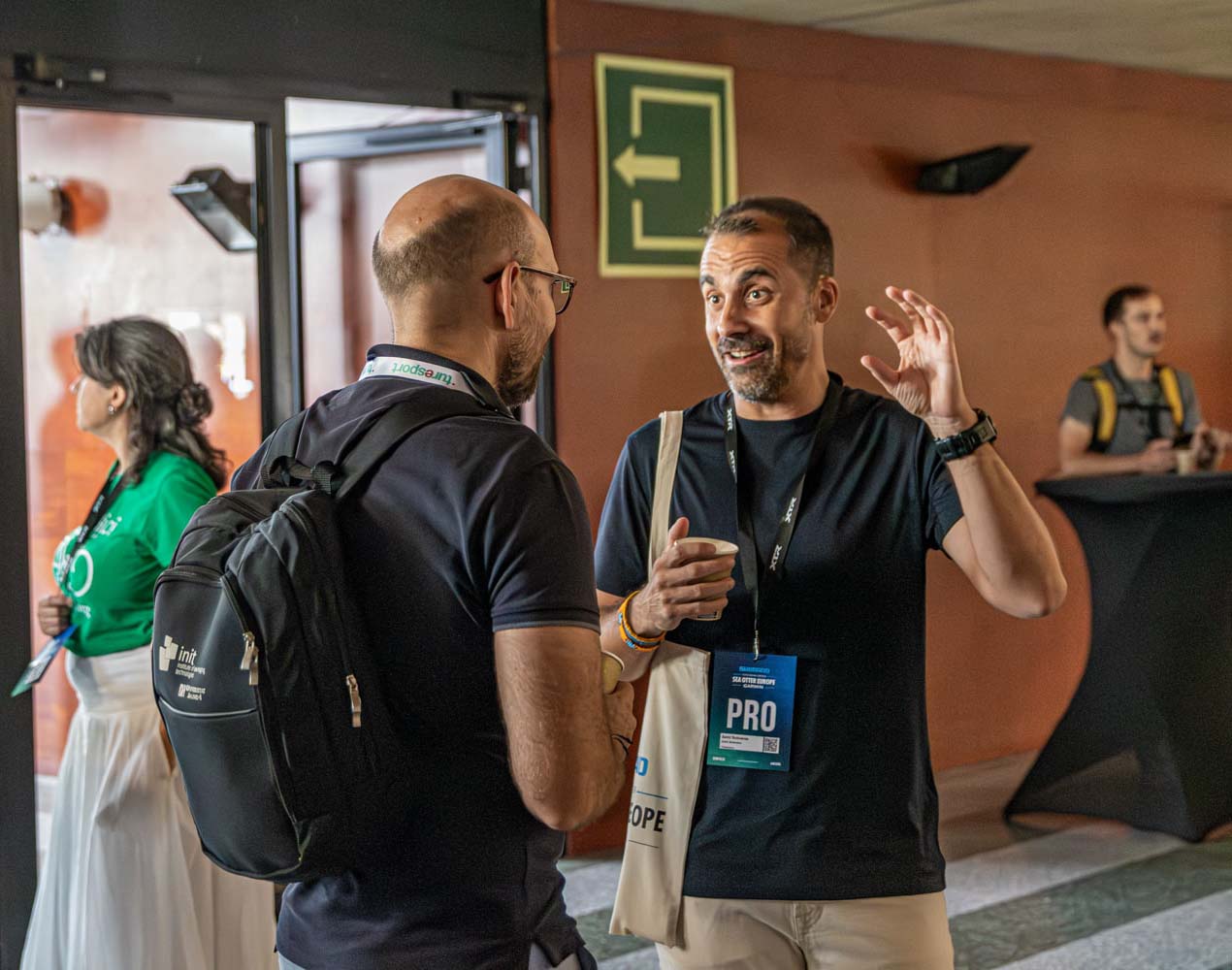 Dos hombres que llevan la acreditación profesional y que han participado en las conferencias Sea Otter Europe Connect realizando networking en el interior del pabellón Fontajau de Girona.